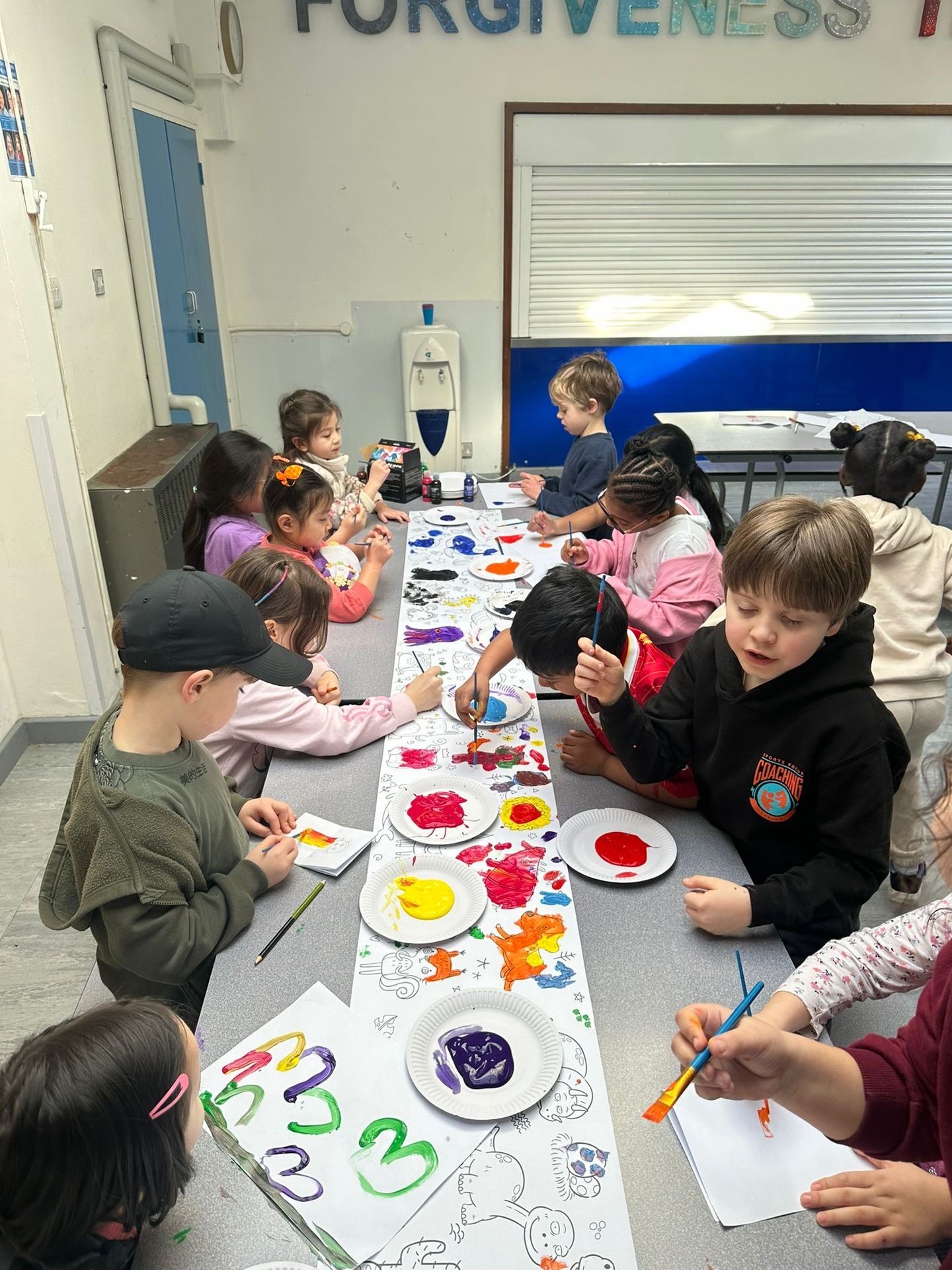 Group of children at school wraparound childcare setting with paints and large cartoon character freize.