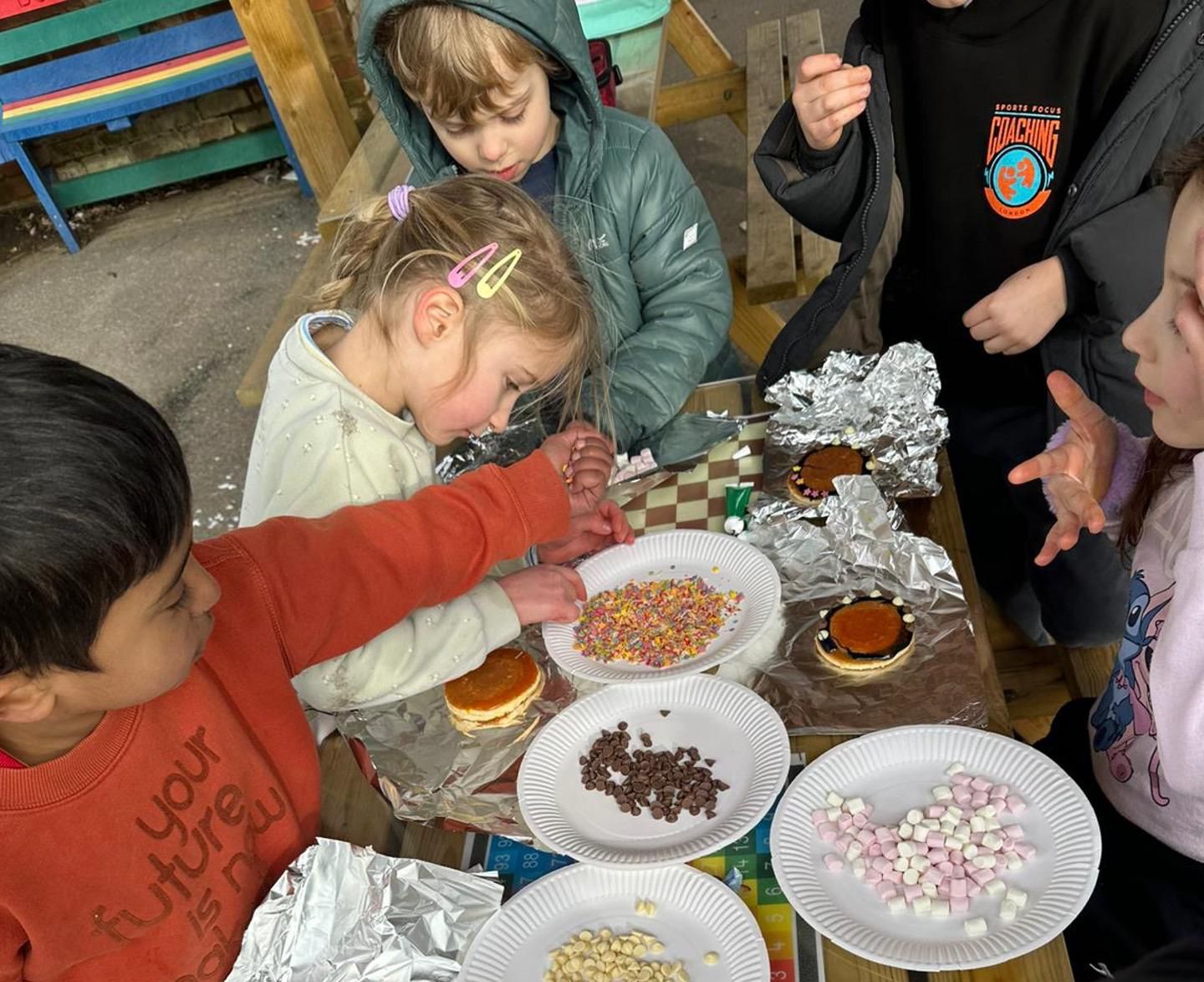 Group of young children at after school wraparound care decorating pancakes with sprinkles and small marshmallows.